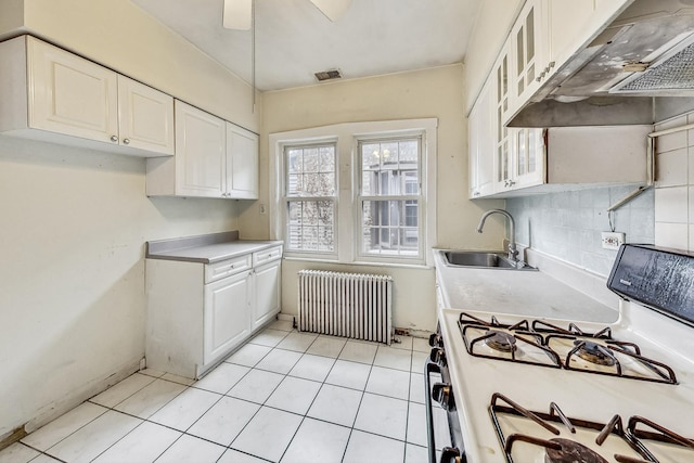 kitchen with radiator, sink, white range with gas cooktop, light tile patterned flooring, and white cabinetry