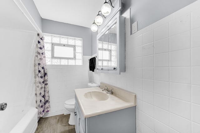 full bathroom featuring toilet, wood-type flooring, vanity, shower / tub combo with curtain, and tile walls