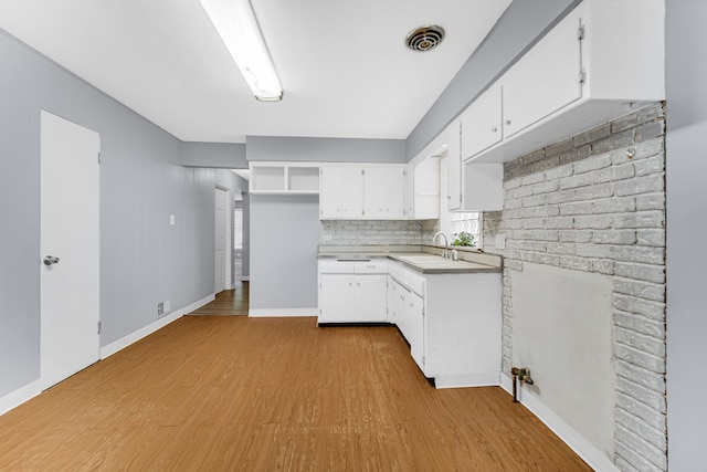 kitchen with tasteful backsplash, sink, a fireplace, white cabinetry, and light hardwood / wood-style floors