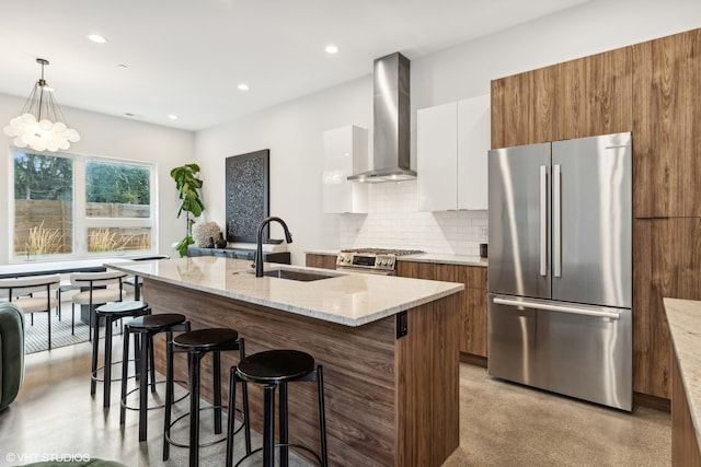 kitchen featuring a center island with sink, appliances with stainless steel finishes, white cabinetry, wall chimney exhaust hood, and sink