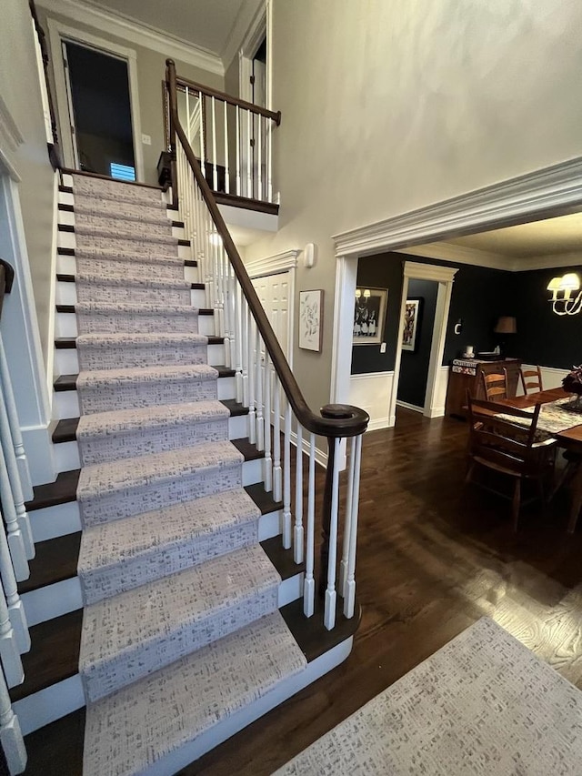 stairway with wood-type flooring, ornamental molding, and a chandelier