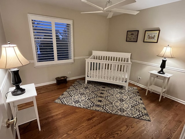 bedroom with ceiling fan, a nursery area, and dark hardwood / wood-style floors