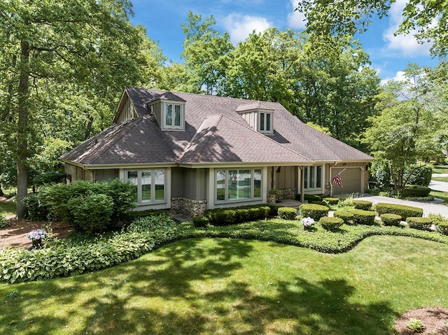 cape cod home with a shingled roof, stone siding, an attached garage, a front lawn, and brick siding