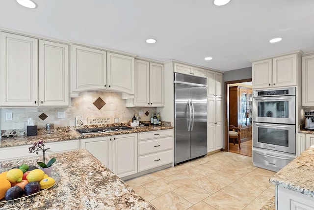 kitchen featuring light stone counters, stainless steel appliances, white cabinetry, backsplash, and a warming drawer