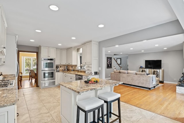 kitchen featuring light stone countertops, stainless steel appliances, a breakfast bar area, and white cabinets