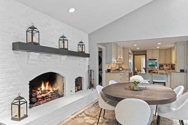 dining area featuring lofted ceiling, stacked washer and dryer, a fireplace, and recessed lighting