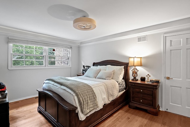 bedroom with ornamental molding, light wood-style flooring, visible vents, and baseboards