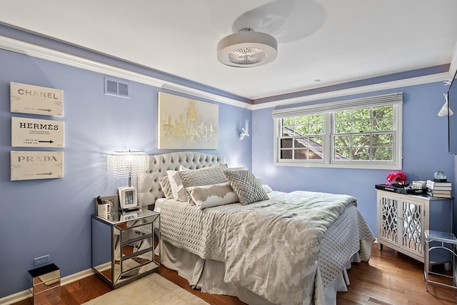 bedroom with crown molding, wood finished floors, visible vents, and baseboards