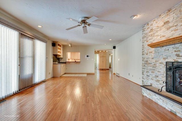 unfurnished living room featuring ceiling fan, light wood-type flooring, a fireplace, and a textured ceiling