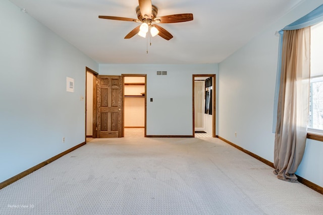 unfurnished bedroom with ceiling fan, light colored carpet, a closet, and a walk in closet