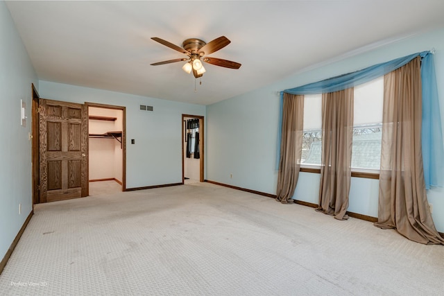 unfurnished bedroom featuring a spacious closet, light colored carpet, a closet, and ceiling fan