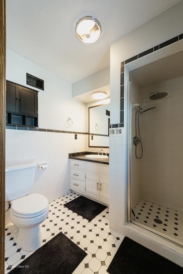 bathroom with tile walls, toilet, vanity, and a tile shower