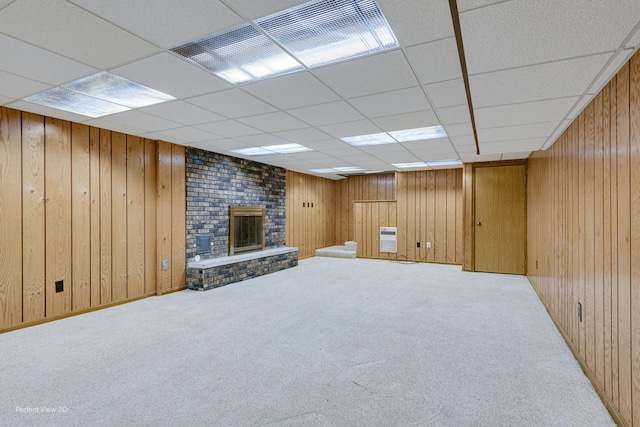 basement with a brick fireplace, a drop ceiling, carpet floors, and wooden walls