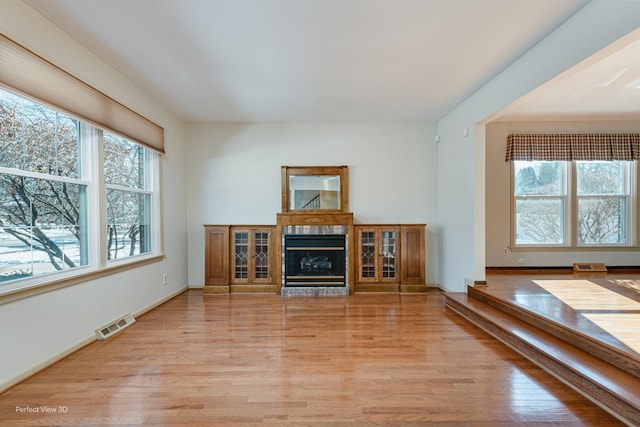 unfurnished living room with a wealth of natural light, light hardwood / wood-style flooring, and a tiled fireplace