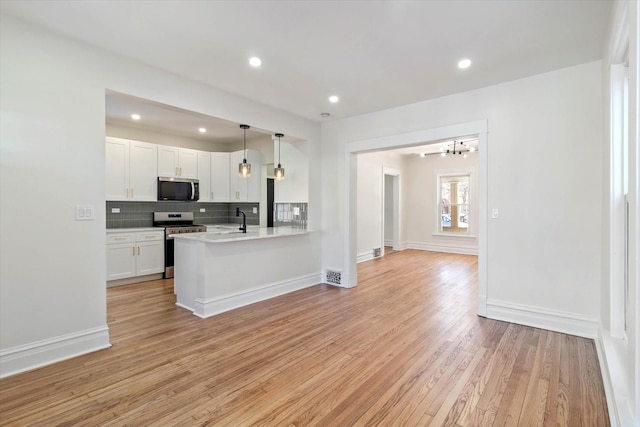 kitchen featuring stainless steel appliances, light countertops, hanging light fixtures, white cabinetry, and a peninsula