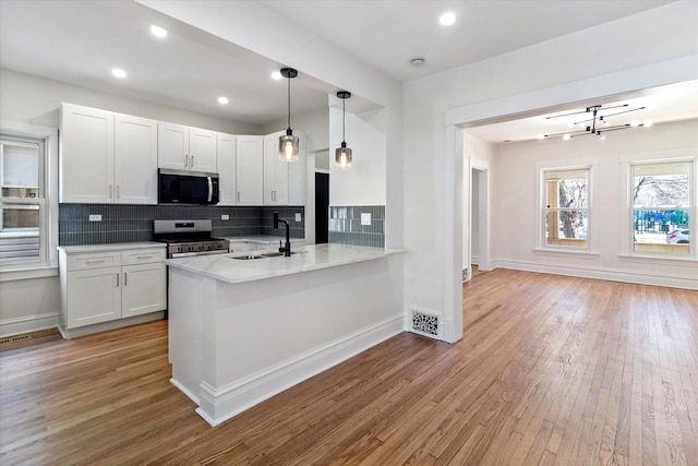 kitchen with pendant lighting, appliances with stainless steel finishes, white cabinetry, a sink, and a peninsula