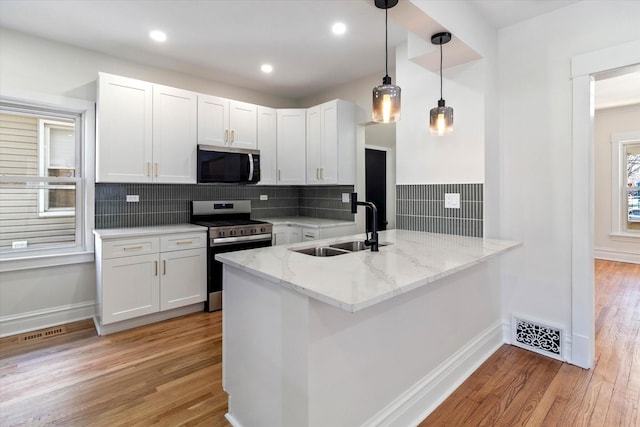 kitchen with decorative light fixtures, appliances with stainless steel finishes, white cabinetry, a sink, and a peninsula