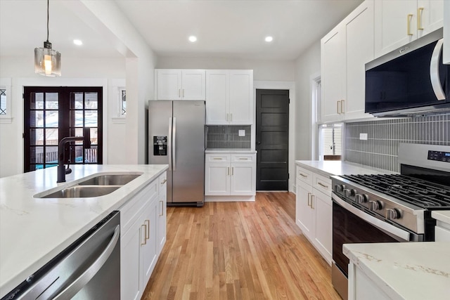 kitchen with stainless steel appliances, white cabinetry, a sink, and decorative light fixtures