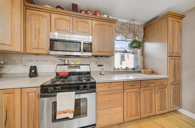 kitchen with appliances with stainless steel finishes, light hardwood / wood-style flooring, and tasteful backsplash