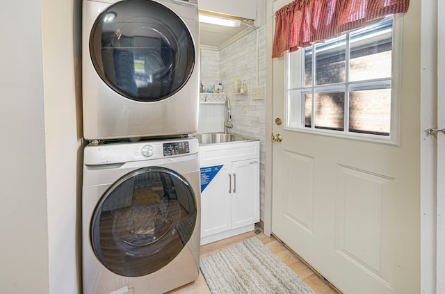 laundry room with sink, stacked washer / drying machine, and cabinets