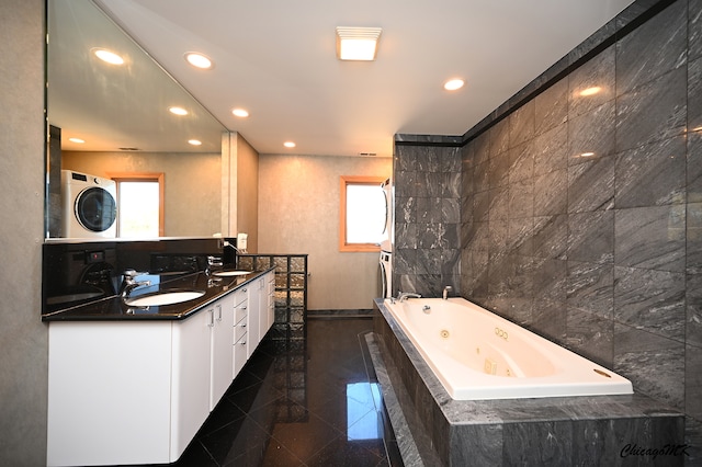 bathroom with stacked washing maching and dryer, tile patterned floors, vanity, tile walls, and tiled bath