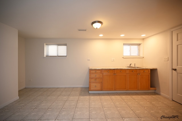 kitchen with light tile patterned floors, light stone counters, plenty of natural light, and sink