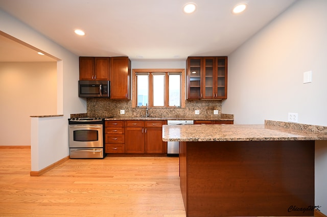 kitchen featuring kitchen peninsula, backsplash, appliances with stainless steel finishes, and light wood-type flooring