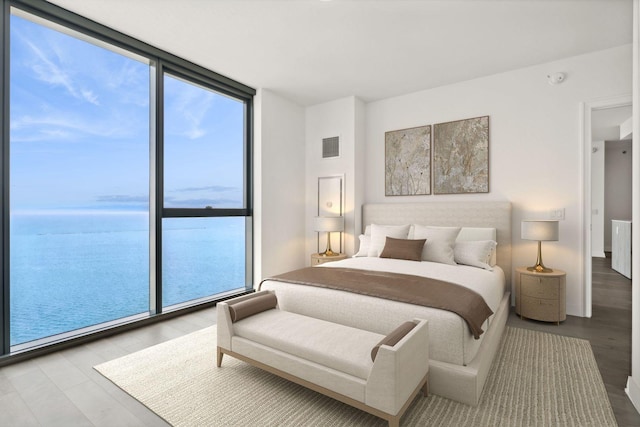 bedroom featuring floor to ceiling windows, a water view, and hardwood / wood-style flooring