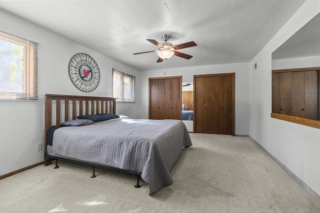 carpeted bedroom featuring ceiling fan, a textured ceiling, and two closets