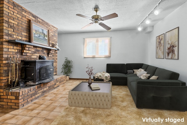 living room with ceiling fan, a textured ceiling, a wood stove, and light tile patterned floors