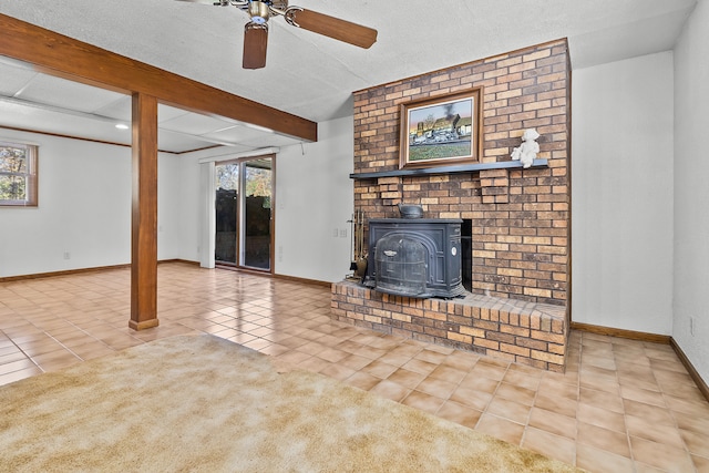 unfurnished living room featuring a wood stove, a textured ceiling, ceiling fan, beamed ceiling, and light tile patterned floors