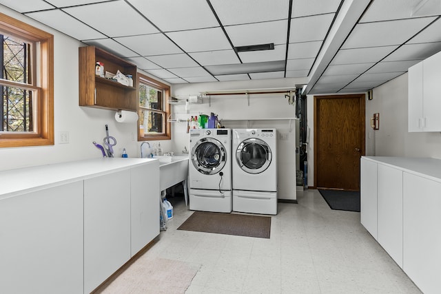 clothes washing area featuring a wealth of natural light, washer and dryer, and cabinets