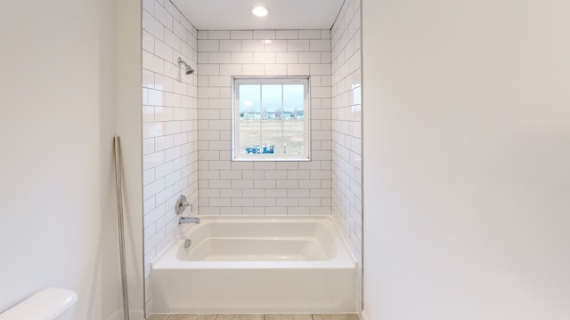 bathroom with toilet, tiled shower / bath combo, and tile patterned flooring