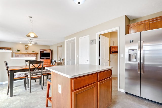 kitchen featuring a kitchen island, stainless steel fridge with ice dispenser, pendant lighting, a fireplace, and ceiling fan