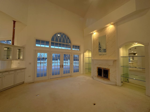 unfurnished living room with a high end fireplace, french doors, light colored carpet, and high vaulted ceiling