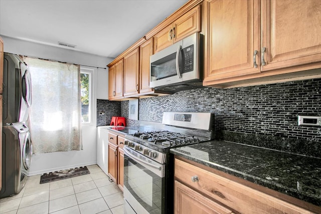 kitchen featuring tasteful backsplash, stacked washing maching and dryer, dark stone counters, light tile patterned flooring, and stainless steel appliances