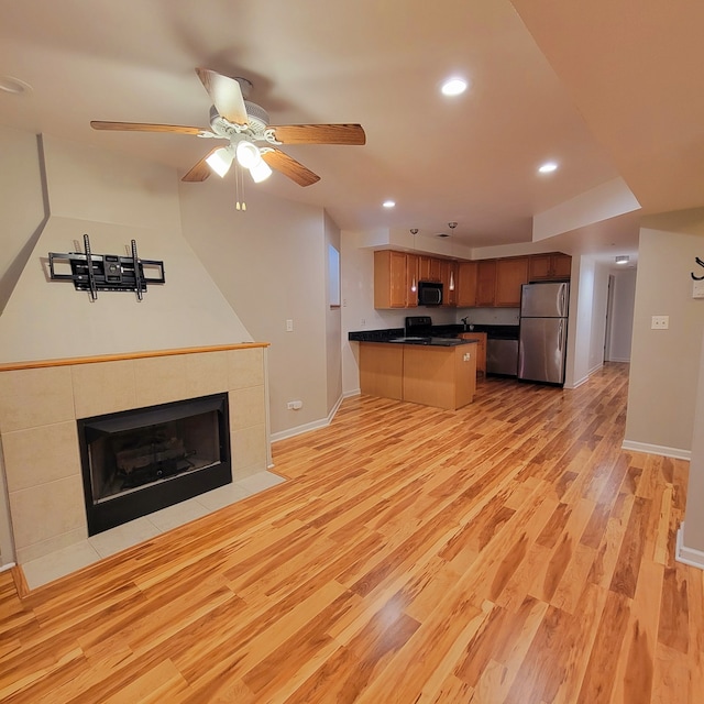 kitchen featuring ceiling fan, black appliances, light hardwood / wood-style flooring, and a fireplace