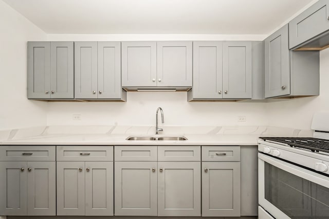 kitchen featuring gray cabinets, sink, light stone countertops, and white gas range oven