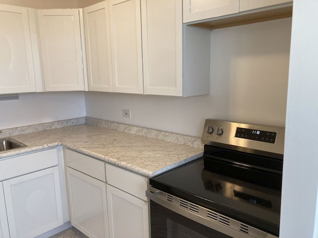 kitchen with white cabinetry, stainless steel electric range oven, light stone counters, and sink