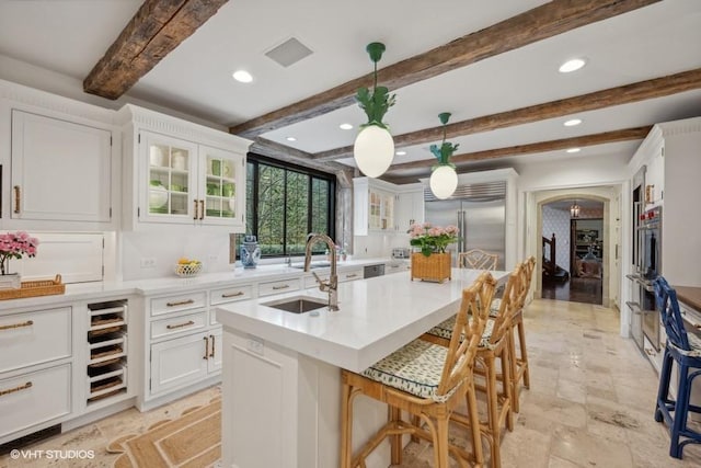 kitchen with sink, white cabinetry, built in refrigerator, hanging light fixtures, and a center island with sink