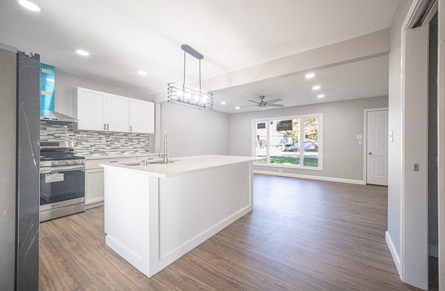 kitchen with dark hardwood / wood-style floors, wall chimney exhaust hood, an island with sink, white cabinetry, and stainless steel range oven