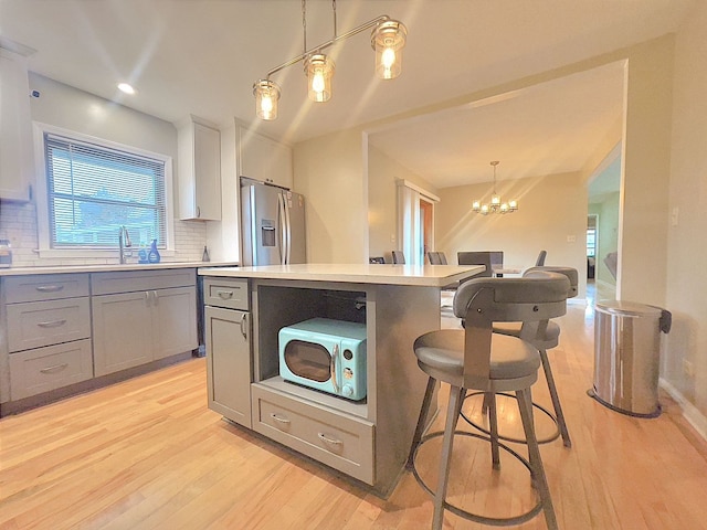 kitchen with pendant lighting, gray cabinetry, backsplash, and stainless steel fridge