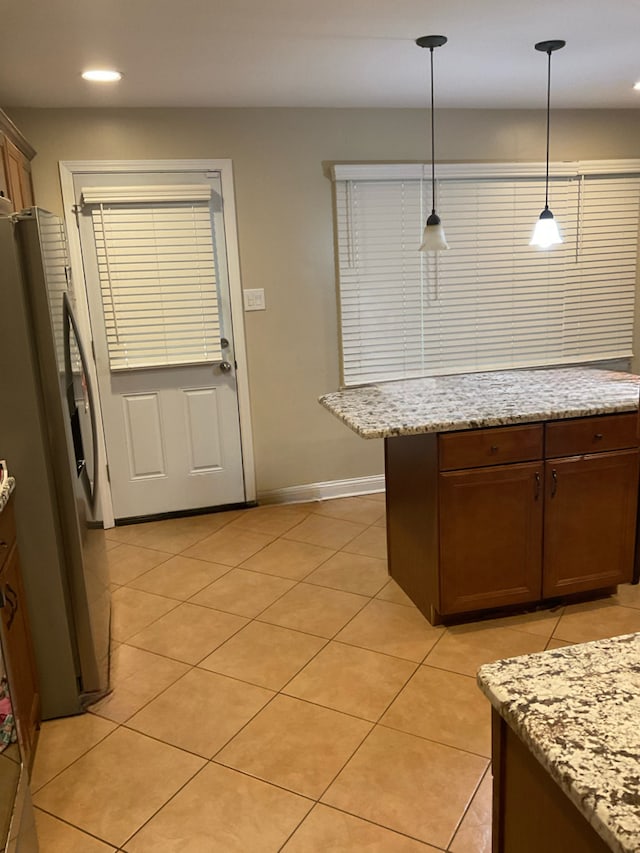 kitchen featuring light stone countertops, stainless steel refrigerator, light tile patterned floors, and hanging light fixtures