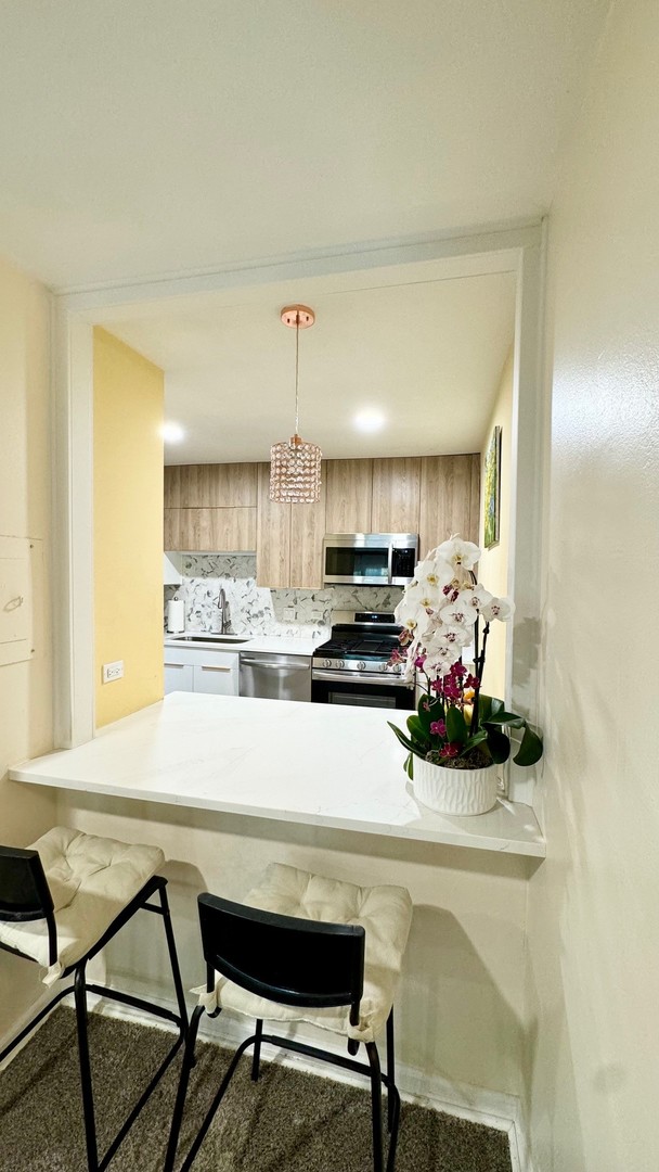 kitchen featuring light brown cabinets, decorative backsplash, a breakfast bar area, appliances with stainless steel finishes, and pendant lighting