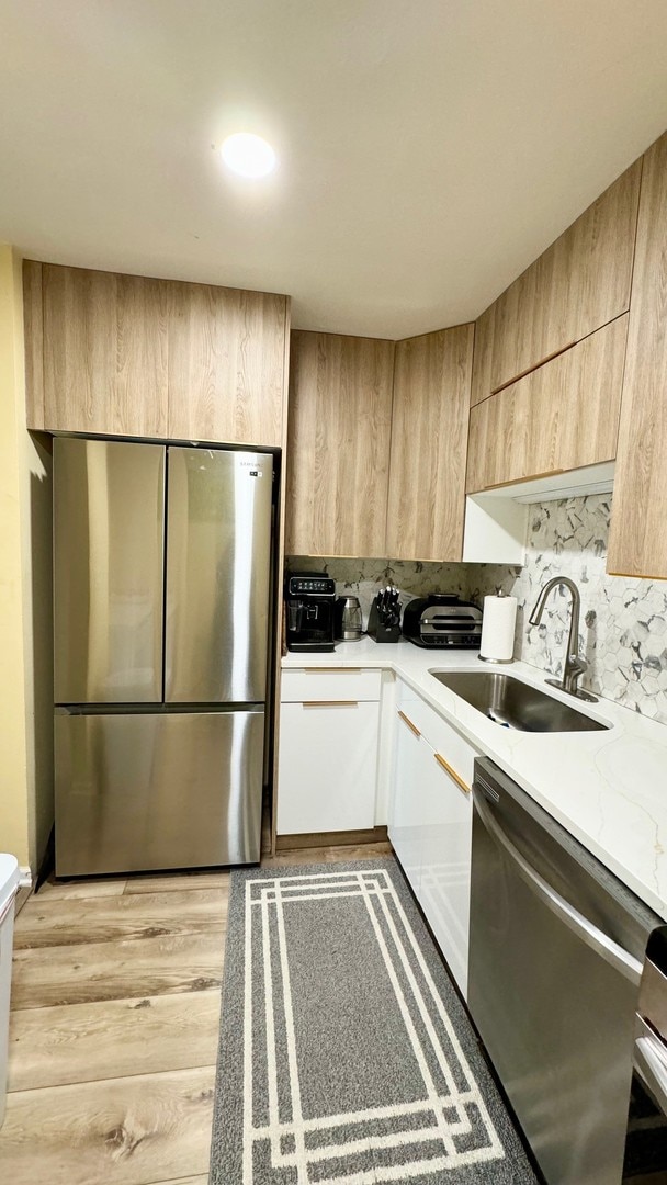 kitchen with decorative backsplash, light brown cabinetry, sink, light hardwood / wood-style floors, and stainless steel appliances