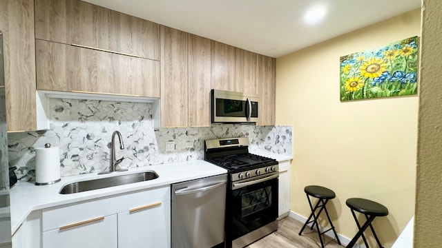 kitchen featuring appliances with stainless steel finishes, sink, white cabinetry, light hardwood / wood-style floors, and decorative backsplash