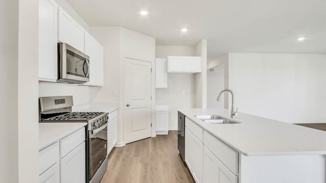 kitchen with white cabinets, an island with sink, appliances with stainless steel finishes, light wood-type flooring, and sink