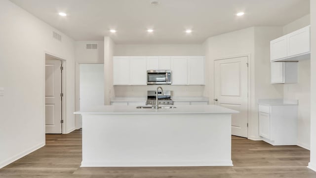 kitchen featuring light hardwood / wood-style floors, white cabinetry, stainless steel appliances, and a center island with sink