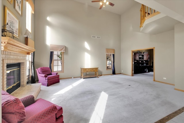 carpeted living room with ceiling fan, a high ceiling, and a brick fireplace