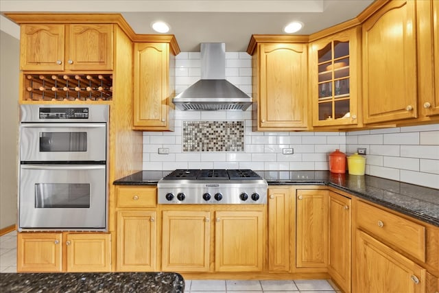 kitchen with tasteful backsplash, stainless steel appliances, wall chimney exhaust hood, dark stone countertops, and light tile patterned floors